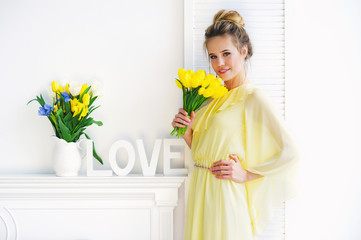 Portrait of a beautiful young woman in yellow dress with spring flowers and white decoration letters