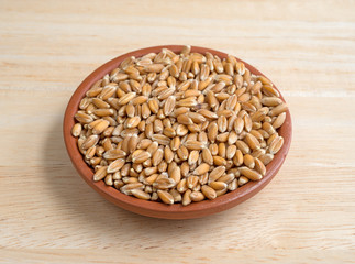 Small bowl filled with organic spelt on a wood table top side view.