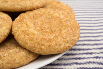 Fresh baked snickerdoodle cookies on a white plate atop a blue striped tablecloth.