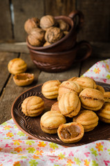 Walnuts shape cookies with condensed milk - dulce de leche in clay bowl on wooden rustic background. Selective focus