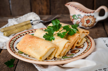 Stuffed russian pancakes rolls with meat in traditional clay bowl on wooden background. Toned image. Selective focus