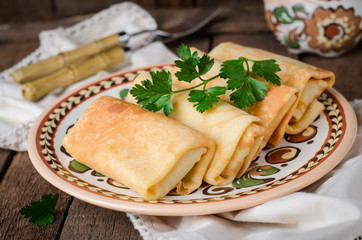Stuffed russian pancakes rolls with meat in traditional clay bowl on wooden background. Toned image. Selective focus