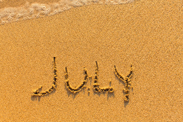 July - written on sandy beach with the soft wave.