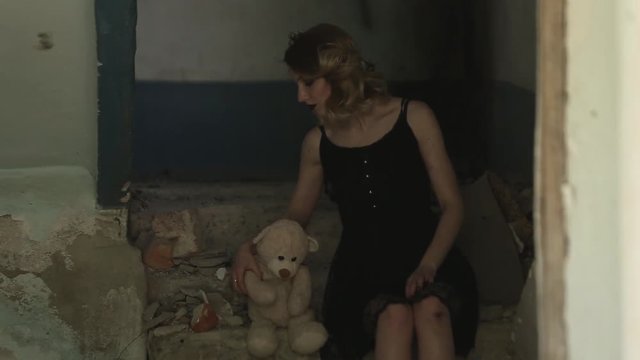 Girl sits in a destroyed room and playing with toy