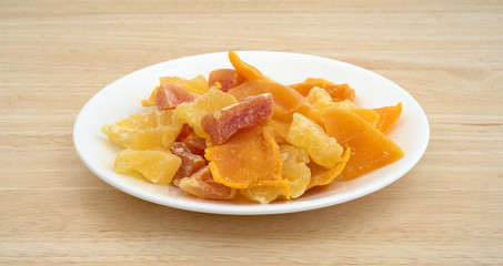 Plate of sugared pineapple, mango and papaya on a wood table top side view.