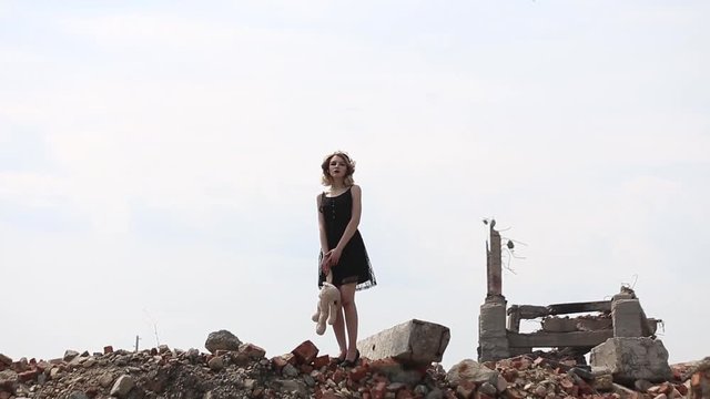 girl in a black dress with a toy bear goes on destruction of buildings