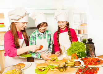 Three young cooks preparing hamburgers at kitchen