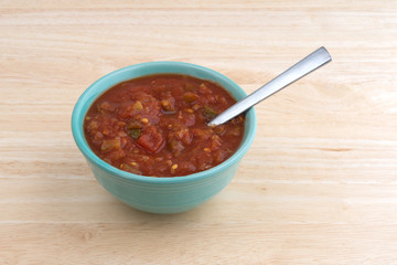 Bowl of chunky salsa sauce with spoon on a table.