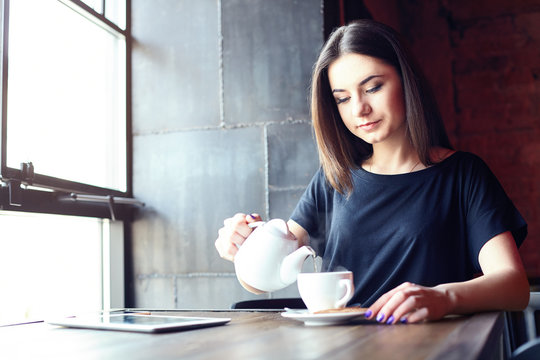 Portrait of young attractive girl pouring tea in coffee shop while sitting alone in coffee shop during free time. Lifestyle, coffee.