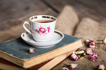 Books, flowers and cup of tea on wooden table with sackcloth