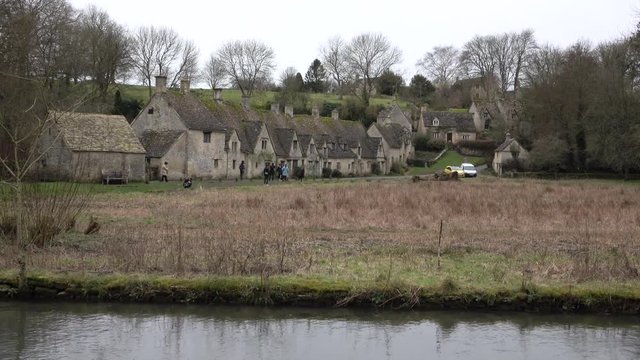 Tourists explore Cotswolds Bibury England river cottages. Historical village homes business. Cotswolds, Area of Outstanding Natural Beauty (AONB) rolling hills and rivers. Destination for tourism
