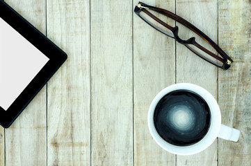 Tablet eyeglasses and a cup of coffee on wood pattern background