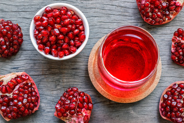 The pomegranate juice in a glass with pieces of pomegranate and pomegranate seeds in a white bowl on wooden background.