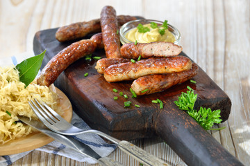 Nürnberger Rostbratwürste mit Senf auf einem rustikalen Steakbrett mit Sauerkraut  serviert -...