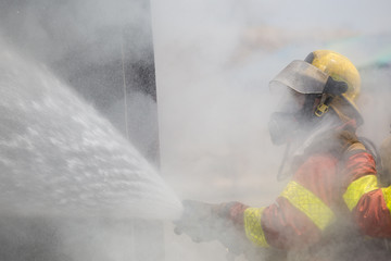 Fototapeta premium fireman in fire fighting suit spraying under smoke and drizzle