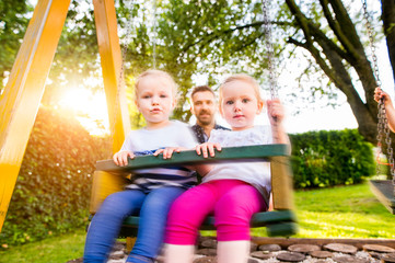 Fototapeta na wymiar Father pushing his daughters on swing in a park.