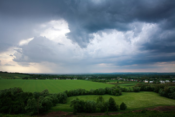 Fototapeta na wymiar Summer village in green fields on background of storm clouds sky