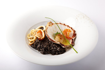Black risotto with seafood served in a shell on a white background