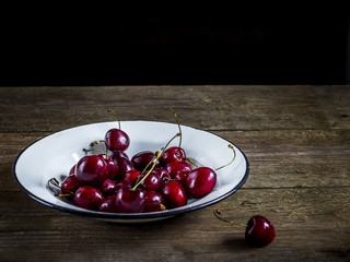 Sweet cherry in white bowl on wooden table.