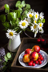 Still life with camomile flowers in jar, glass with fruit drink,peaches and cherry on the plate.