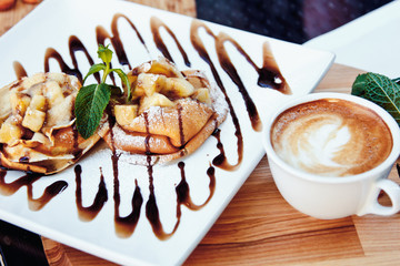 pancakes with chocolate and fruit and coffee on wooden background. Beautiful restaurant serving the dessert