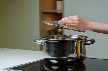 Female hand holding the lid of the pan. Person removing lid from cooking pot.