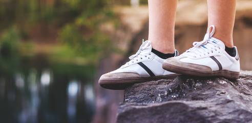 teenager legs in white sneakers on a rock
