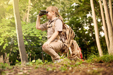 young girl scout, explores  nature with binoculars on camping tr