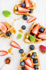 Home made Belgian waffles served on a white woodenl tray with berries , marple syrup and mint leaves