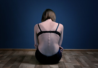 Anorexic girl sitting on the floor on dark wall background