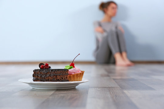 Desperate Woman Sitting On The Floor On Grey Wall Background. Eating Disorder Concept