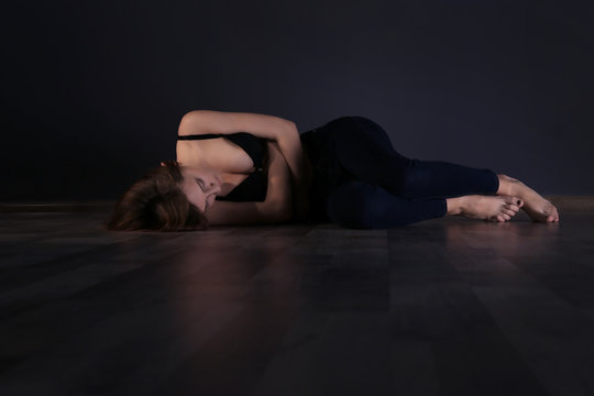 Anorexic girl lying on the floor on dark wall background