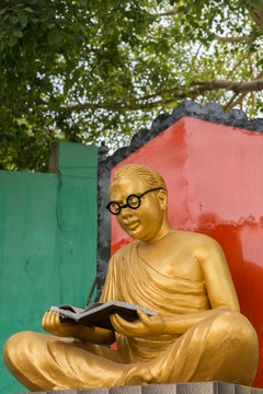 Chettinad, India - October 17, 2013: Golden statue of the actor and politician C.N Annadurai in the Karaikudi City. He reads a book and has black rimmed glasses. Green background.