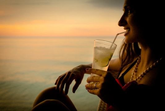 Frau im Sommer Urlaub trinkt Cocktail zum Sonnenuntergang