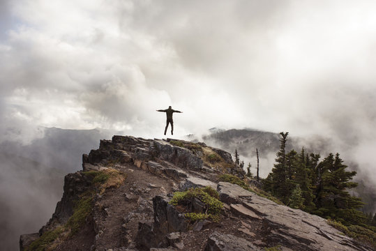 Rear view of man jumping on mountain against cloudy sky