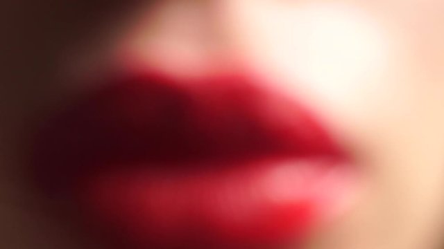 Young woman with beautiful bright red lips kissing a glass at the camera, macro