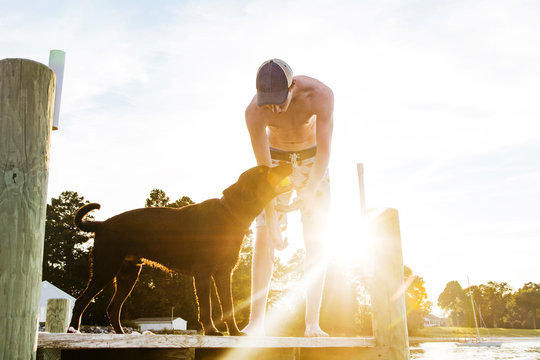 Shirtless Young Man and dog playing with ball on pier during summer