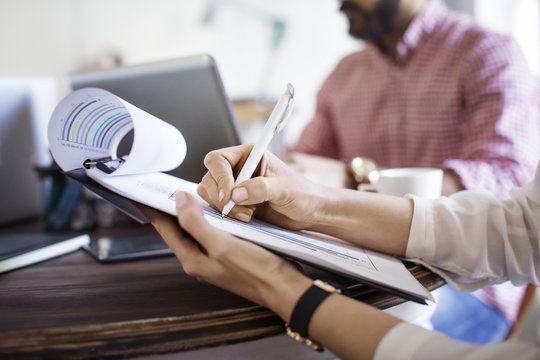 Midsection of businesswoman writing on clipboard during meeting in office