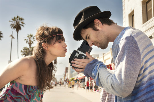 Side view of woman puckering lips while man photographing through vintage camera on sidewalk