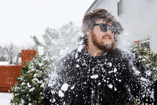 Snow falling on young man standing outside house