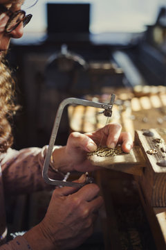 Cropped image of female goldsmith using saw while making jewelry in workshop