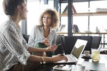 Businesswoman working on laptop while sitting by happy colleague at cafe