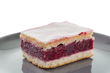 Gedeckter Kirschkuchen mit Zuckerguss auf grauem Teller vor weißem Hintergrund.