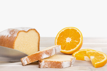 Ein Messer schneidet einen Zitronekuchen mit einigen Orangenfrüchten auf einem Holzbrett.