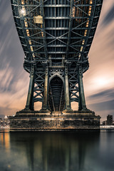 Moody symmetrical perspective under Manhattan Bridge at night.