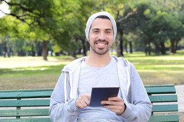 Obraz premium Young man using tablet sitting on park bench.