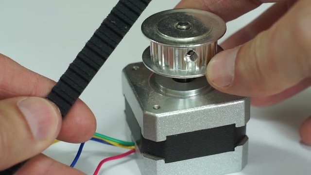 Close up macro shot of a person comparing a cogged belt to a toothed belt pulley hub attached to a small electric stepper motor typically used in robotics and machines that require accurate movements.