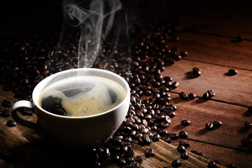 Steaming coffee cup and coffee beans on wood background with copy-space and dark tone.