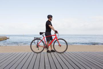 Fototapeta premium Man standing with bike looking at view of a Melbourne beach