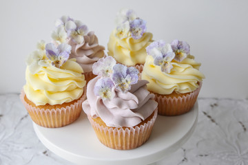 Purple and yellow cupcakes with sugared edible flowers on cake stand